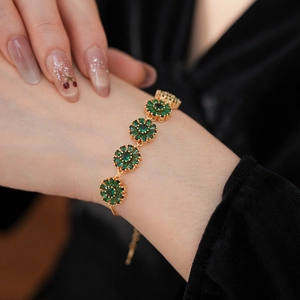 Close-up of vintage emerald green flower zircon bracelet on wrist with gold chain