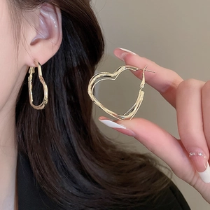 Detail of layered gold hollow heart hoop earrings held for size and texture comparison