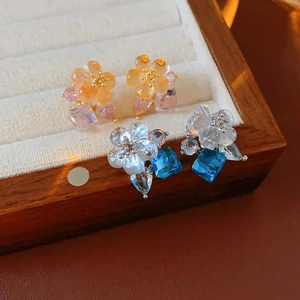 Detailed view of floral zircon earrings with water-drop stones in a wooden jewelry box