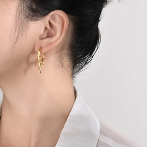 Close-up of golden irregular fluid-shaped drop earrings on model for a modern metal look