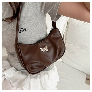 Detail of dark brown pleated shoulder bag with silver butterfly charm on female model