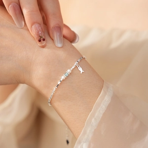 Detail of silver bead bracelet featuring white pearls, blue gem, and a small fish charm