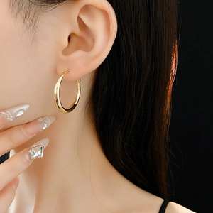 Close-up of elegant gold hoop earrings worn by a model against a dark background