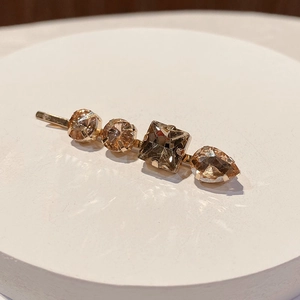 Close-up of golden hair clip with four amber rhinestones in round, square, and teardrop shapes
