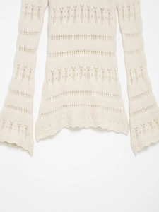 Close-up of cream hollow-out knit sweater featuring flared sleeves and wavy lace hemline