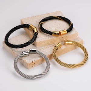 Minimalist stainless steel twisted cable bangles displayed on natural stone platforms