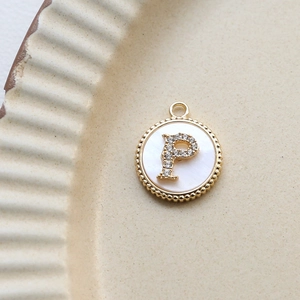 Detail of round gold-plated pendant with shell inlay and zircon letter P on ceramic plate
