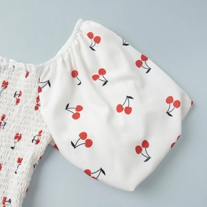 Detail of puff sleeves and elastic smocking on a white dress with red cherry print