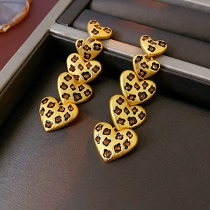 Detailed macro view of gold leopard print heart dangle earrings in a grey jewelry box