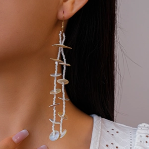 Detailed view of long tassel shell earrings with white glass beads and golden hooks