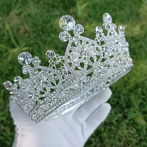 Baroque silver bridal crown with sparkling crystals held in gloved hand on green lawn