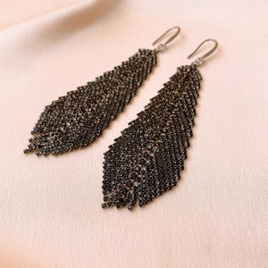Detailed view of leaf tassel earrings with black rhinestones on a soft beige fabric background