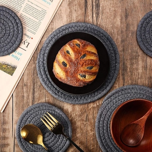 Thick round woven grey cotton heat-resistant place mat on dark wood background