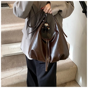 Brown leather hobo bag held by model on stairs with a small doll charm detail