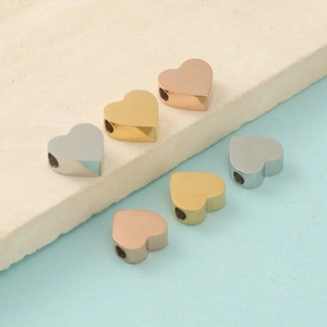 Polished heart beads in gold, silver, and rose gold finishes on a minimalist background