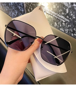 Detail of oversized black frame sunglasses with dark grey lenses and a white leather case