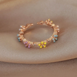 Close-up of pastel flower ring with colorful drip oil petals and zircon on satin fabric