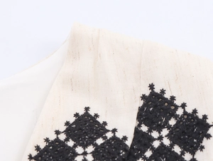Macro detail of black geometric embroidery on cream linen fabric of a V-neck dress