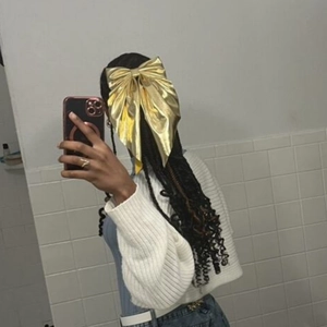 Macro shot of large golden bow hair clip with flowing ribbons on black wavy hair