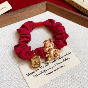 Gros plan sur chouchou en satin rouge avec breloque cheval dorée et symbole de chance