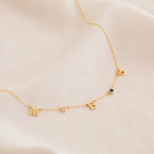 Detalle de un collar dorado con iniciales M, B, S y piedras de nacimiento de colores vivos