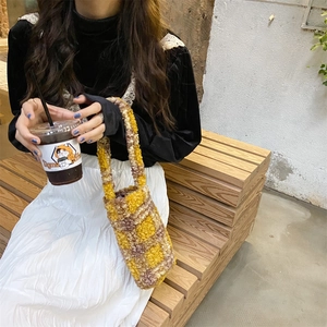 Detail of yellow and brown checkered plush handbag on a wooden bench outdoors
