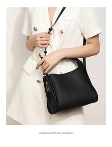 Detail of black lychee leather bucket bag with gold hardware on white blazer model