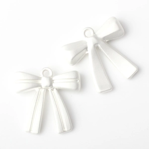 Macro shot of two white matte bow pendants with small hanging rings for DIY jewelry