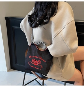Detail of black nylon tote with red cherry embroidery and checkered bow shoulder strap