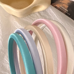 Close-up of padded satin headbands in assorted pastel colors on a minimal background