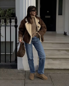 Gros plan sur une veste en peau lainée marron avec jean bleu et accessoires en daim