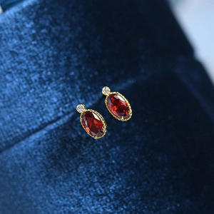 Macro shot of vintage gold stud earrings with oval red gems and white zircon accents