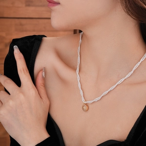 Detail of multi-strand pearl necklace featuring a gold starburst pendant on model