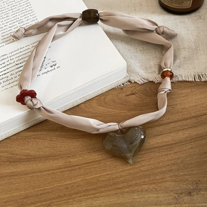 Detail of vintage beige fabric bow necklace with a large grey-green heart resin pendant