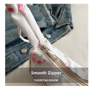 Close-up of smooth silver metal zipper on white floral crescent bag with denim background