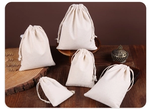 Detail view of five different sizes of natural cotton drawstring storage pouches on wood