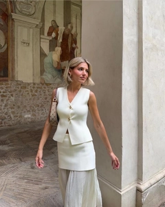 Détail d'un ensemble gilet en tricot blanc à boutons dorés et jupe plissée