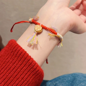 Gros plan d'un bracelet en corde tressée rouge avec pendentif cœur doré et pompons