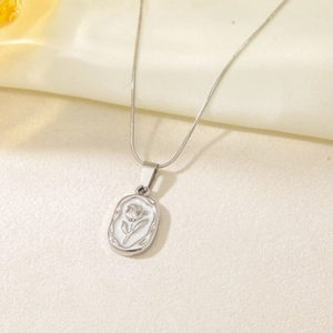 Close-up of silver tulip flower relief pendant on a delicate chain over silk fabric