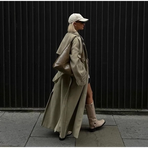 Close-up of olive wool coat paired with a brown leather tote bag and beige accessories