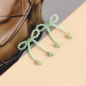 Detail of mint green beaded bow earrings with dangling beads on a peach background