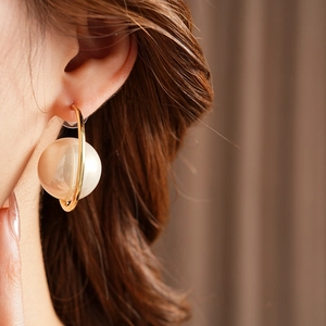 Close-up of a model wearing a gold C-shaped earring with a white pearl accent