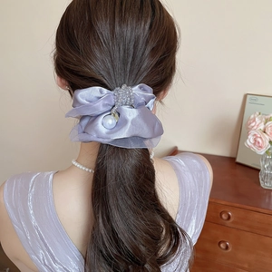 Detail of lavender satin hair scrunchie with pearls worn on model's hair in a cozy setting