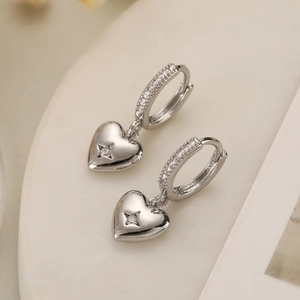 Dettaglio macro di orecchini a cuore argentati con stella in zircone e finitura lucida