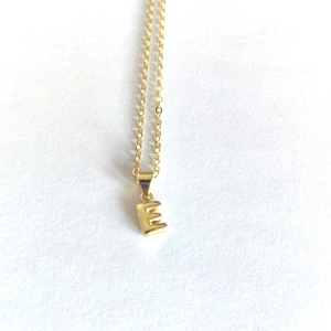 Close-up of golden letter E pendant on delicate chain with a high-polished finish