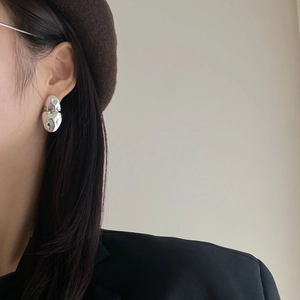 Polished silver irregular geometric stud earrings worn by a model in a minimal setting
