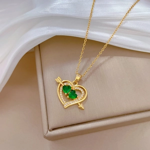 Close-up of gold heart necklace with green gems and crystals on white silk