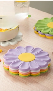 Stackable daisy silicone heat-resistant mats in various macaron colors on a wood table