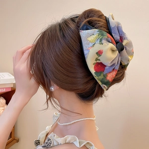Detailed view of floral fabric bow clip with vintage oil painting print and metal logo