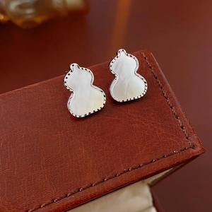Detailed view of silver gourd-shaped stud earrings with white inlay on brown leather box